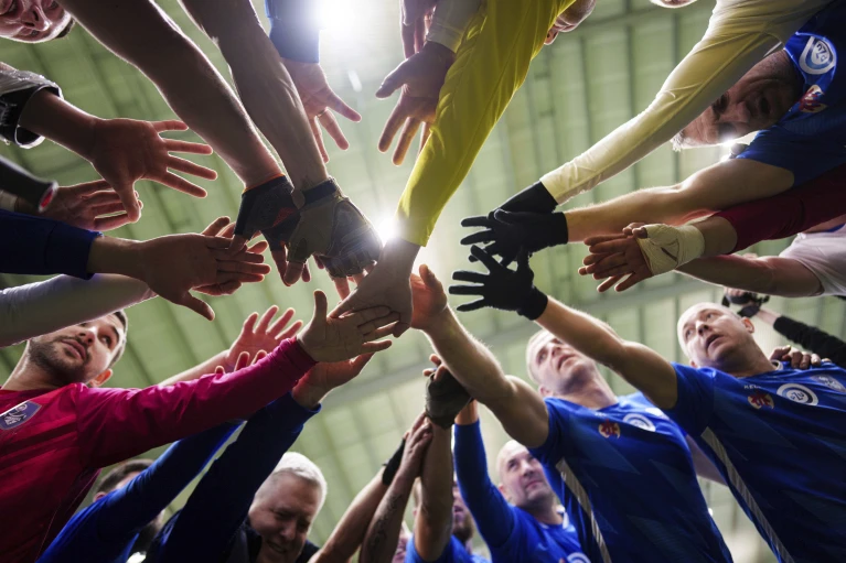 Футболісти ФК «Покрова» та ФК «Покрова-2» тягнуть руки назустріч один одному під час першого українського футбольного турніру для поранених у війні з ампутаціями кінцівок у Києві, Україна, 11 січня 2025 року.